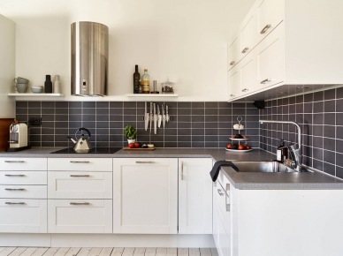 Biała kuchnia skandynawska z czarnymi płytkami pomiędzy szafkami i półkami na ścianie (25613)