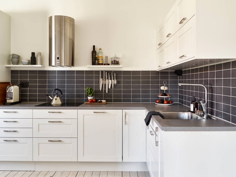 Biała kuchnia skandynawska z czarnymi płytkami pomiędzy szafkami i półkami na ścianie