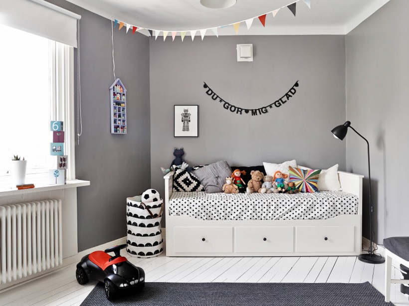 Białe łóżko z szufladami,szara ściana,kolorowe proporczyki girlanda,białe deski na podłodze i biało-czarne dekoracje w pokoju dziecięcym