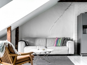 Szara sofa o prostej formie wydaje się idealnie komponować z ciekawą aranżacją wokół. Pasiasty dywan oraz poduszki...