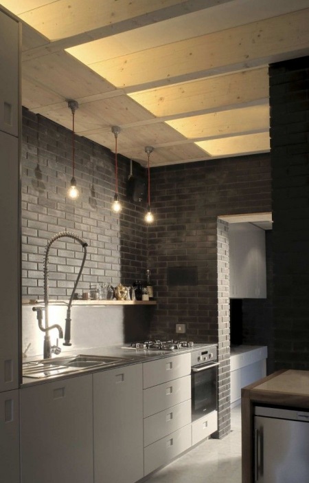 Nowoczesna szara kuchnia z ciemnoszarą cegłą na ścianie, drewnianym sufitem i żarówkami na kablach