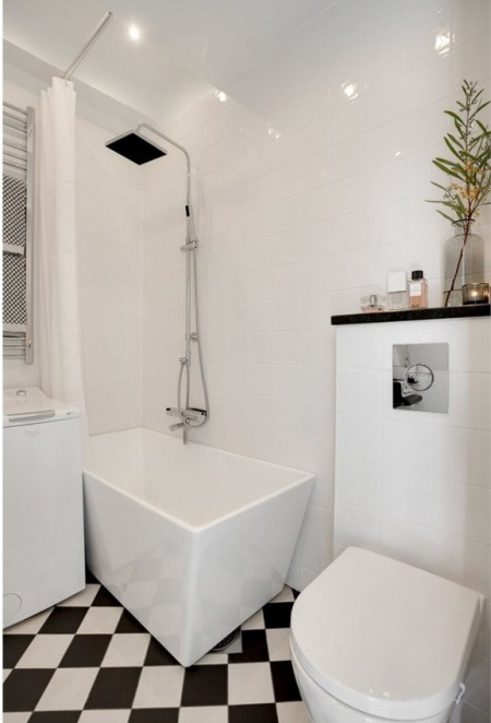 Prostokątna nowoczesna wanna z deszczownią, czarno-biała terakota ułożona w karo i nowoczesne punktowe oświetlenie sufitowe w białej łazience