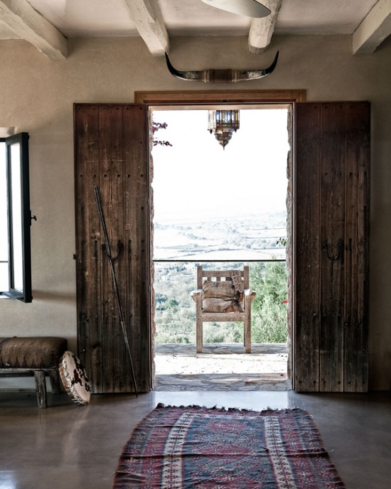 Ciemnobrązowe drewniane drzwi wrota z okuciami z żelaza, betonowe ściany i etniczny dywanik