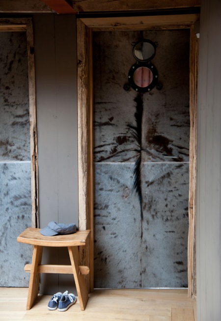 Pomysłowe drzwi z drewna i szarego futerka z metalowym okragłym okienkiem w korytarzu z szarymi ścianami