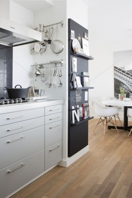 Czarna ściana z wąskimi półeczkami w białej kuchni nowoczesnej