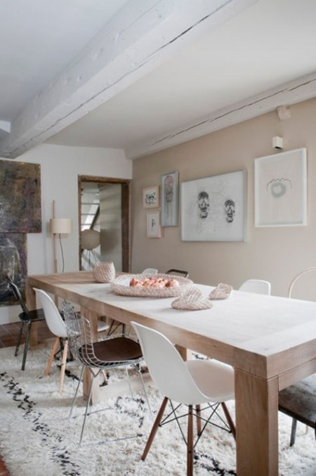 Prostokątny nowoczesny stół z naturalnego drewna z drucianymi   i białymi krzesłami vitra ,tkany dywan berberyjski i nowoczesne grafiki na ścianach