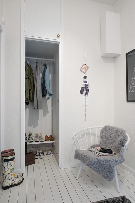 Mała garderoba we wnęce w przedpokoju,biały drewniany fotel skandynawski,biale malowane deski na podłodze