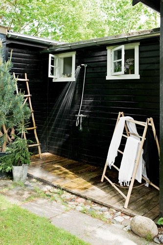 Deszczownia natrysk i drewniane wieszaki drabinki na zewnątrz małego czarnego domku w stylu skandynawskim