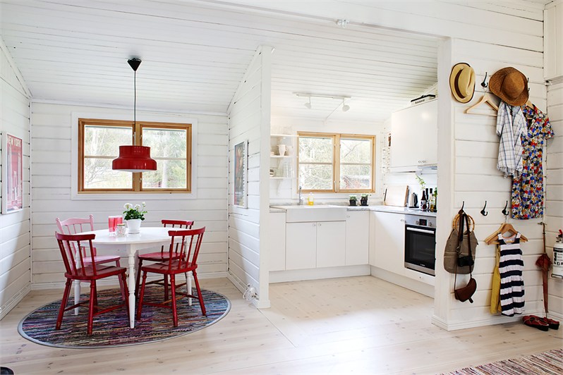 Mała biała kuchnia z jadalnią z okrągłym stołem i czerwonymi krzesłami z drewna