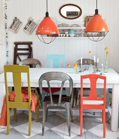 Różnokolorowe krzesła w mieszanym stylu przy  białym stole w jadalni z pomarańczowymi przemysłowymi lampami