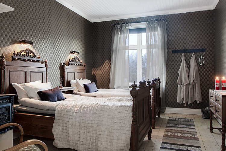 Stylowe rzeźbione łóżka z drewna w skandynawskiej sypialni z podłogą z surowych desek i tkanym dywanikiem