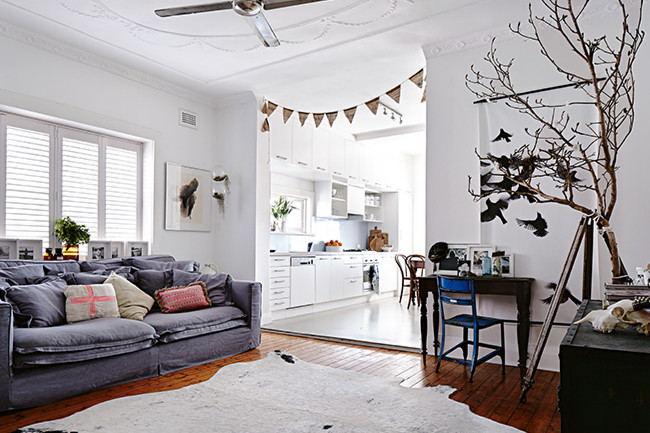 Szara sofa,bydlęca biała skóra na podłodze,niebieskie krzesło,proporczyki i biała kuchnia w otwaretej przestrzeni mieszkania