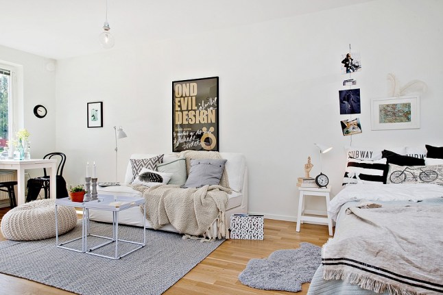 Czarno-białe poduszki na łóku stojącym w salonie z białymi stolikami,białą sofą i szarym dywanem