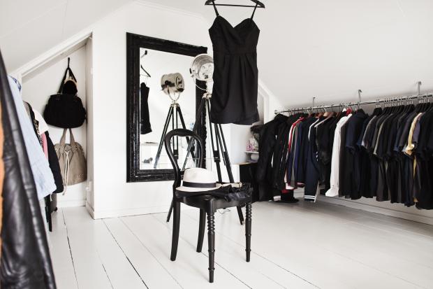 Czarne stylowe lustro na białej ścianie w garderobie z odkrytymi wieszakami,czarne giete krzesło na białych deskach podłogi