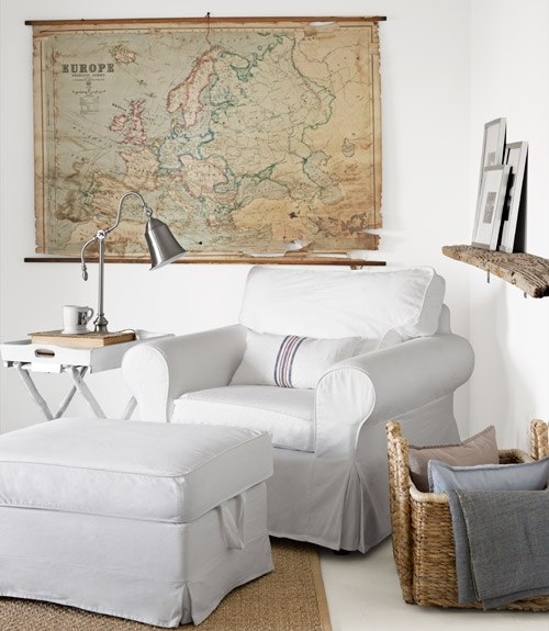 Dekoracyjna mapa Europy, biały fotel  i drewniana półka w aranżacji salonu