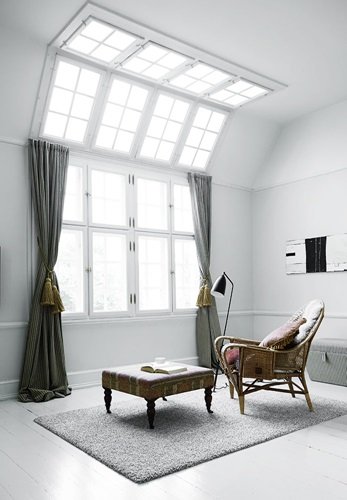 Duże okna z sufitowym swietlikie,mietowe zasłony z chwostami,etniczny puf i wiklinowy fotel w skandynawskim salonie