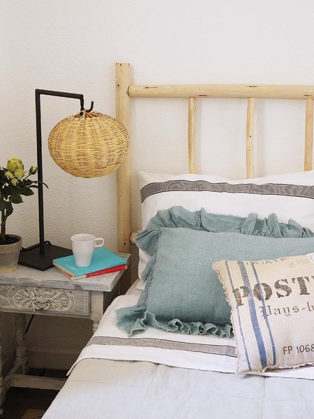 Rama łóżka z drewnianej żerdzi,metalowa lampka z plecionym abażurem,poduszki z falbankami i poduszki  industrialne z napisami,stylowy bielony stolik nocny
