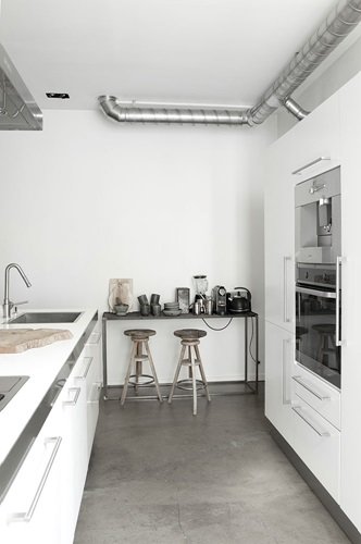 Betonowa posadzka, drewniane stołki i industrialna konsolka w białej kuchni
