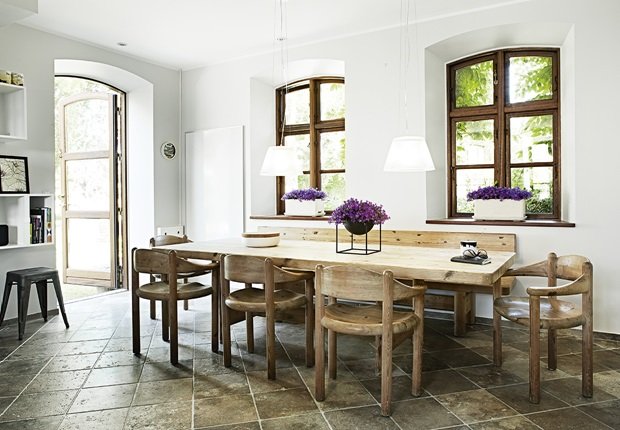 Drewniane klasyczne okna w białej jadalni z drewnianym stołem z ławka i krzesłami na kamiennej posadzce