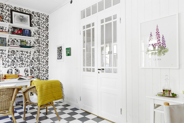 Francuskie drzwi dwuskrzydłowe,biale póli na ścianie z biało-czarną tapetą,podłoga w szachownicę i biały stół z wiklinowymi fotelikami