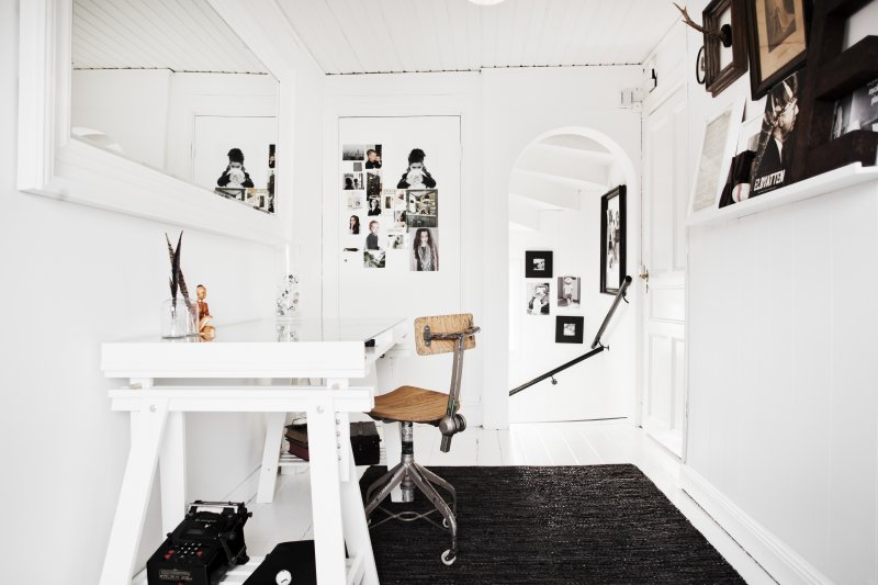 Białe lustro w prostokątnych ramach,białe biurko skandynawskie na kozłach,białe wąskie półeczki ścienne na dekoracje,czarny dywan na białej podłodze
