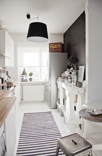 Pomysl na wąską kuchnię z tablicową czarną ścianą,białą konsolą na kozłach w stylu skandynawskim