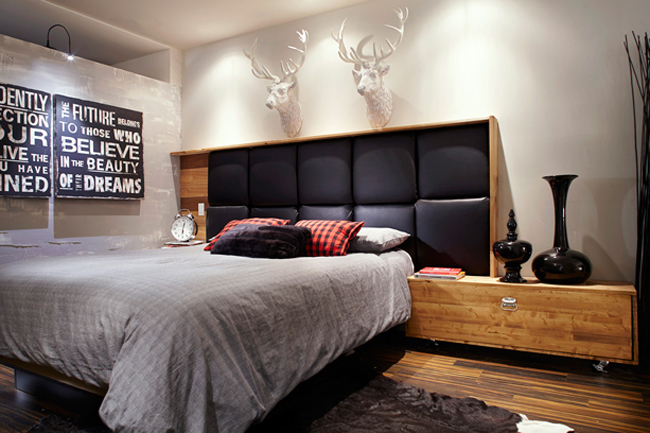 Nowoczesne drewniane łóżko z czarnym pikowanym zagłówkiem, typografie i białe głowy jelonków w męskiej sypialni