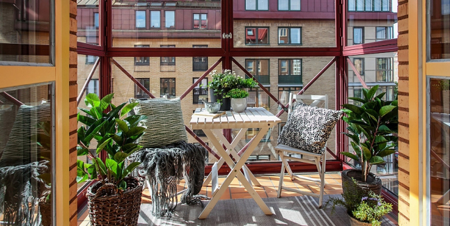 Białe meble i wiklinowe osłonki na rosliny na małym balkonie