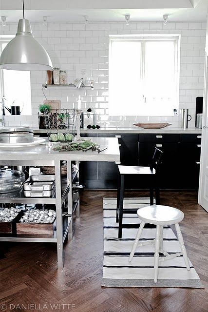 Biała płytka cegiełka na ścianie w kuchni z czarnymi szafkami i metalową wyspą z półkami