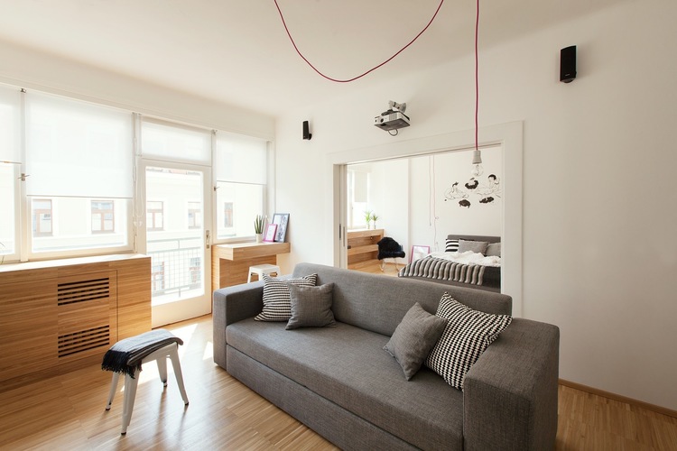 Szara sofa, drewniana zabudowa i różowe kable w salonie w stylu nowoczesnym