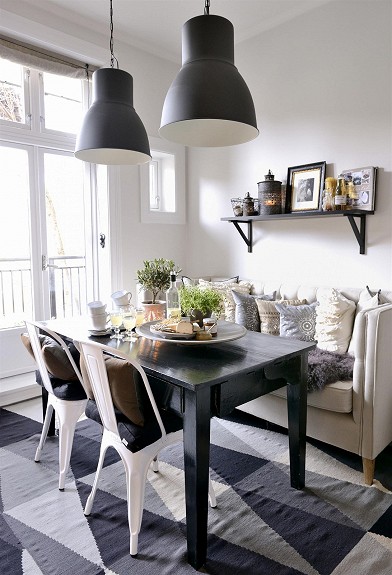 Czarne lampy pendant,czarny stół,białe industrialne krzesła i kanapa z poduchami w jadalni