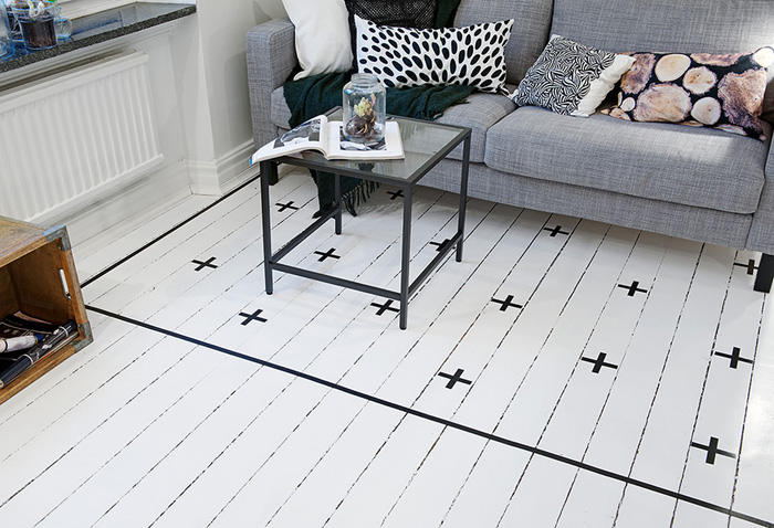 Białe malowane deski z czarnym wzorem szwedzkim zamiast dywanu koło sofy