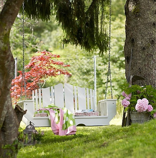 Ogrodowa huśtawka - biała ławka wisząca pomiędzy drzewami