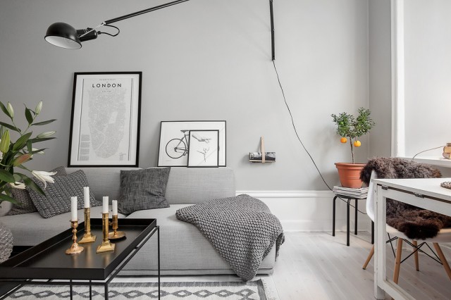 Skandynawskie grafiki,czarny stolik kawowy z tacą blatem,biało-czarny dywan skandynawski i biała podłoga w szarym salonie