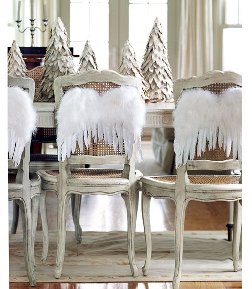 Pierzaste białe skrzydełka aniołowe na prowansalskich krzesła przy sjadalnianym stole światecznym z dekoracyjnymi ośnieżonymi choinkami