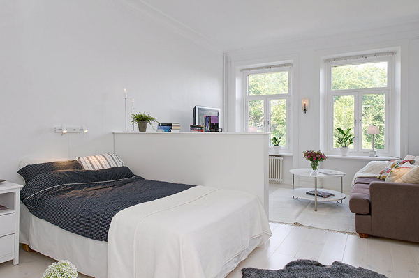 Aneks sypialniany z łózkiem w białym salonie skandynawskim