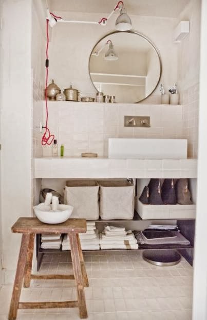 Marokańskie srebrne pojemniki,okragłe lustro,skandynawski kinkiet z wysięgnikiem i drewniany taboret w białej łazience