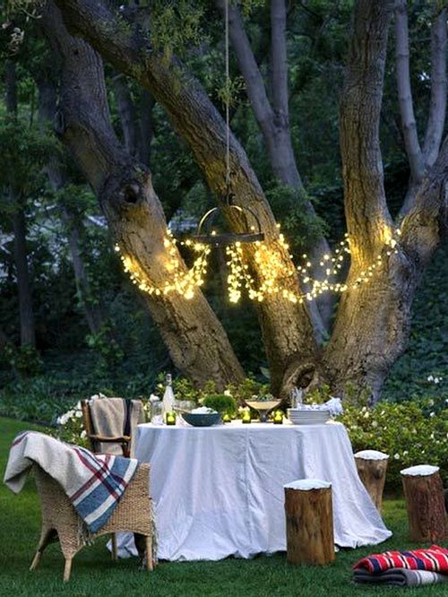 Żyrandol z żarówkowych girland w leśnej aranżacji ogrodu ze stołem