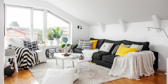 Grafitowa sofa z żółtymi i biało-czarnymi poduszkami,biały stolik,biały futrzak dywan i pld w czarno-białe pasy w dekoracji salonu