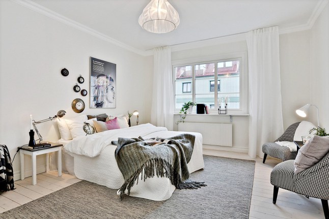 Foteliki z tapicerką w pepitkę,szary tkany dywan,nowoczesne grafiki i kolorowe poduszki na białym łóżku w sypialni skandynawskiej