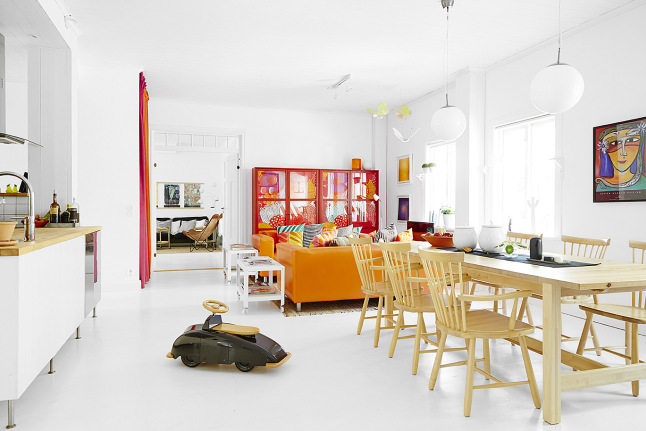 Czerwony regała,pomarańczowa sofa i drewniany stół z krzesłami w otwartym salonie
