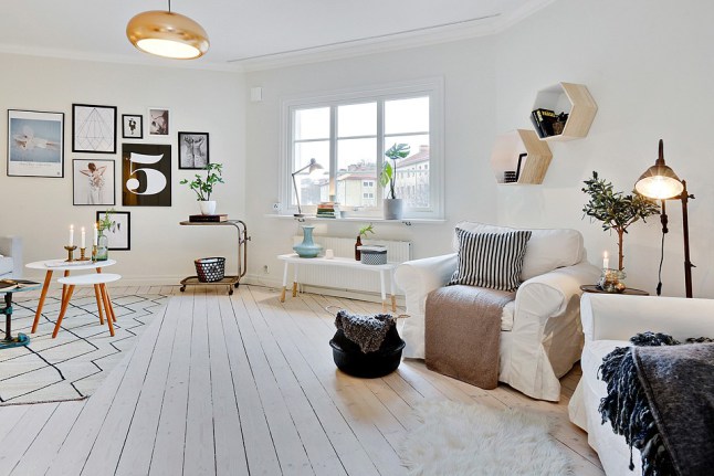 Skandynawskie palakty i grafiki na ścianie w salonie z białymi fotelami i okragłymi stolikami do kawy
