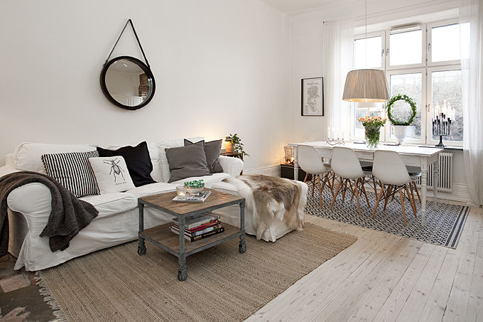 Biała kanapa z poduszkami i skórą w połączeniu z drewnianym stolikiem na kółkach