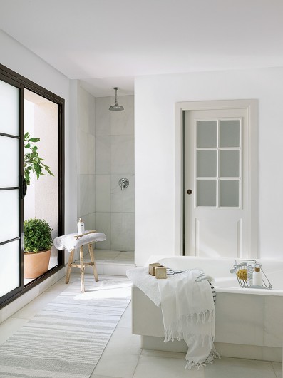 Biała łazienka z dużymi oknami i wanną pośrodku wnętrza