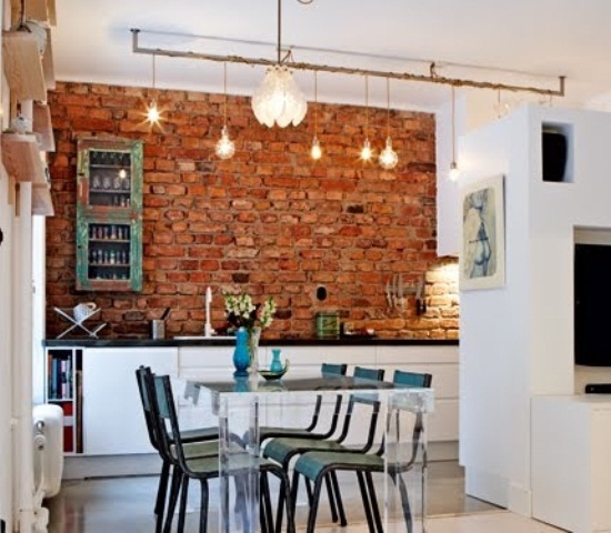 Ekelktyczna kuchnia z nowoczesnym przeźroczystym stołem,industrialnymi turkusowymi krzesłami i szafką w stylu vintage,ścianą z czerwonej cegły i żarówkami na kablu