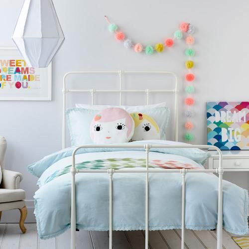 Biała lampa wisząca kokon,girlanda z kolorowych pomponików,kute białe łóżko i kolorowe dekoracyjne poduszki na łóżku