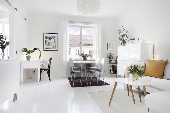 Biały salon skandynawski z jadalnianym stołem i biurkiem przy ścianie