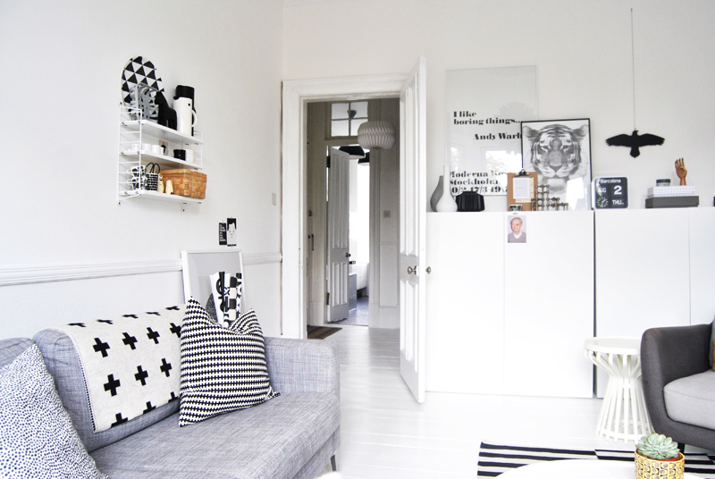 Szara sofa,nowoczesne szafki skandynawskie,białe półki i graficzne poduszki
