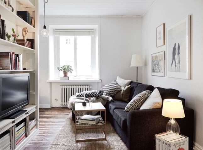 Grafitowa sofa, drewniana postarzana podłoga i biały regała z TV i książkami w małym salonie