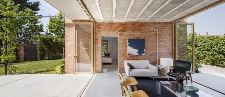 Przeszklony salon z czerwonej cegły z betonową posadzką i składanymi przesuwnymi ścianami ze szkła i drewna